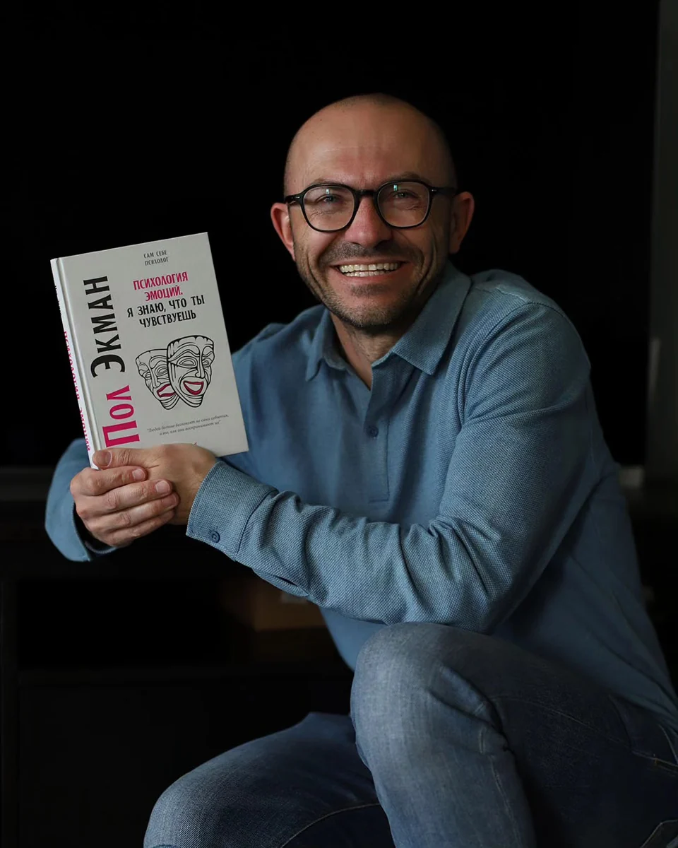 Вадим Лойко улыбается, держа книгу о психологии эмоций
